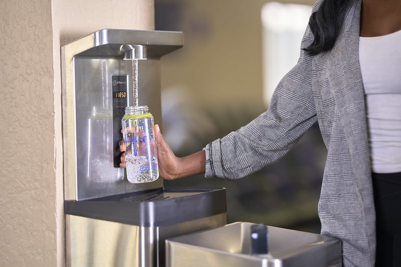 Woman refilling a reusable water bottle at a bottle filling station.