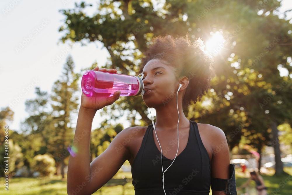 A woman standing outside and drinking out of a pink reusable water bottle.